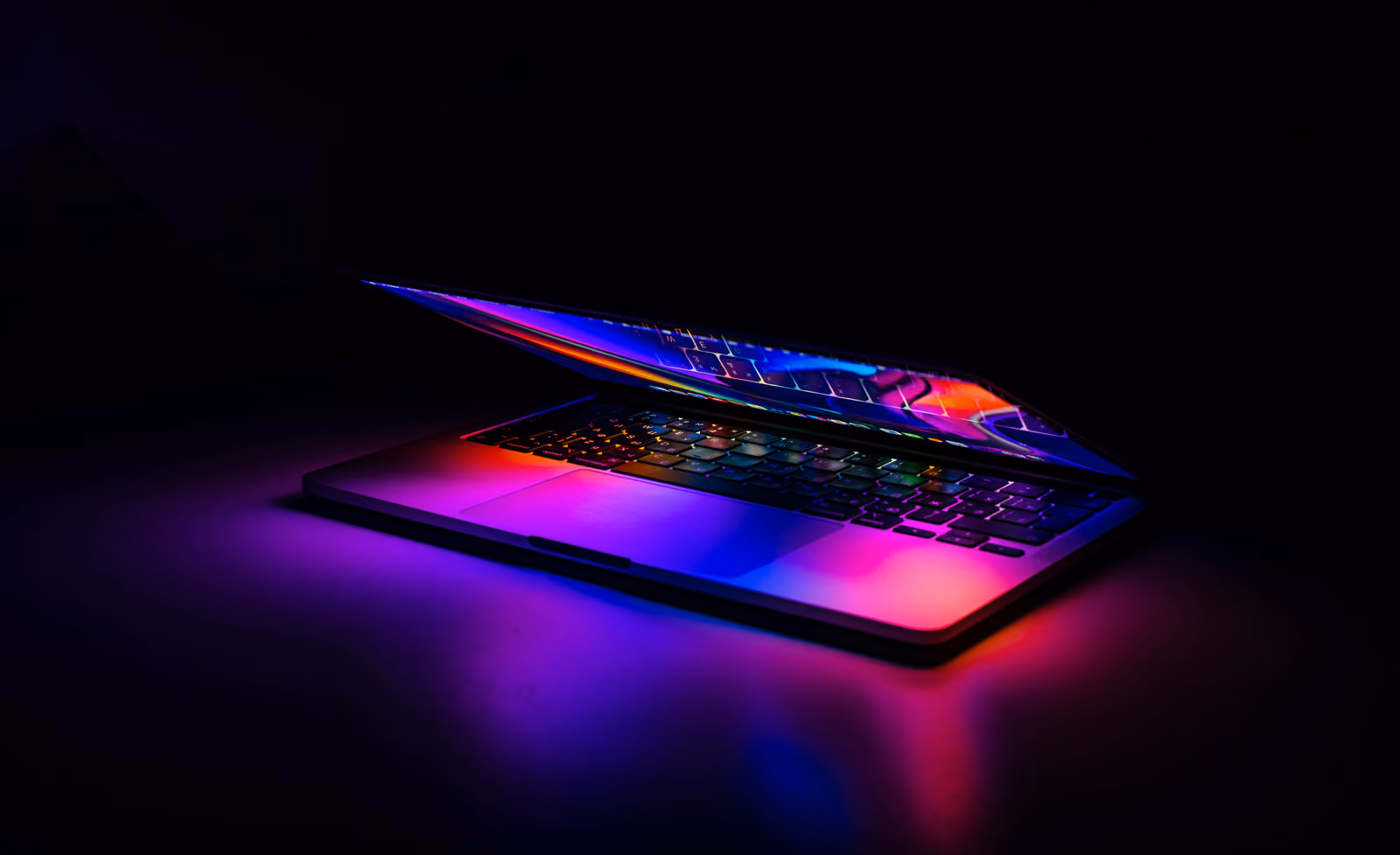 An open laptop lit from beneath by coloured keyboard backlighting in a dark room